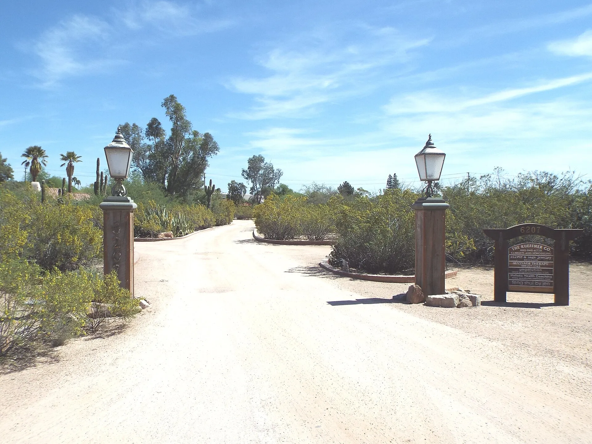 The gated dirt entrance to the Cattle Track Arts Compound in Scottsdale, flanked by lamp posts and desert trees