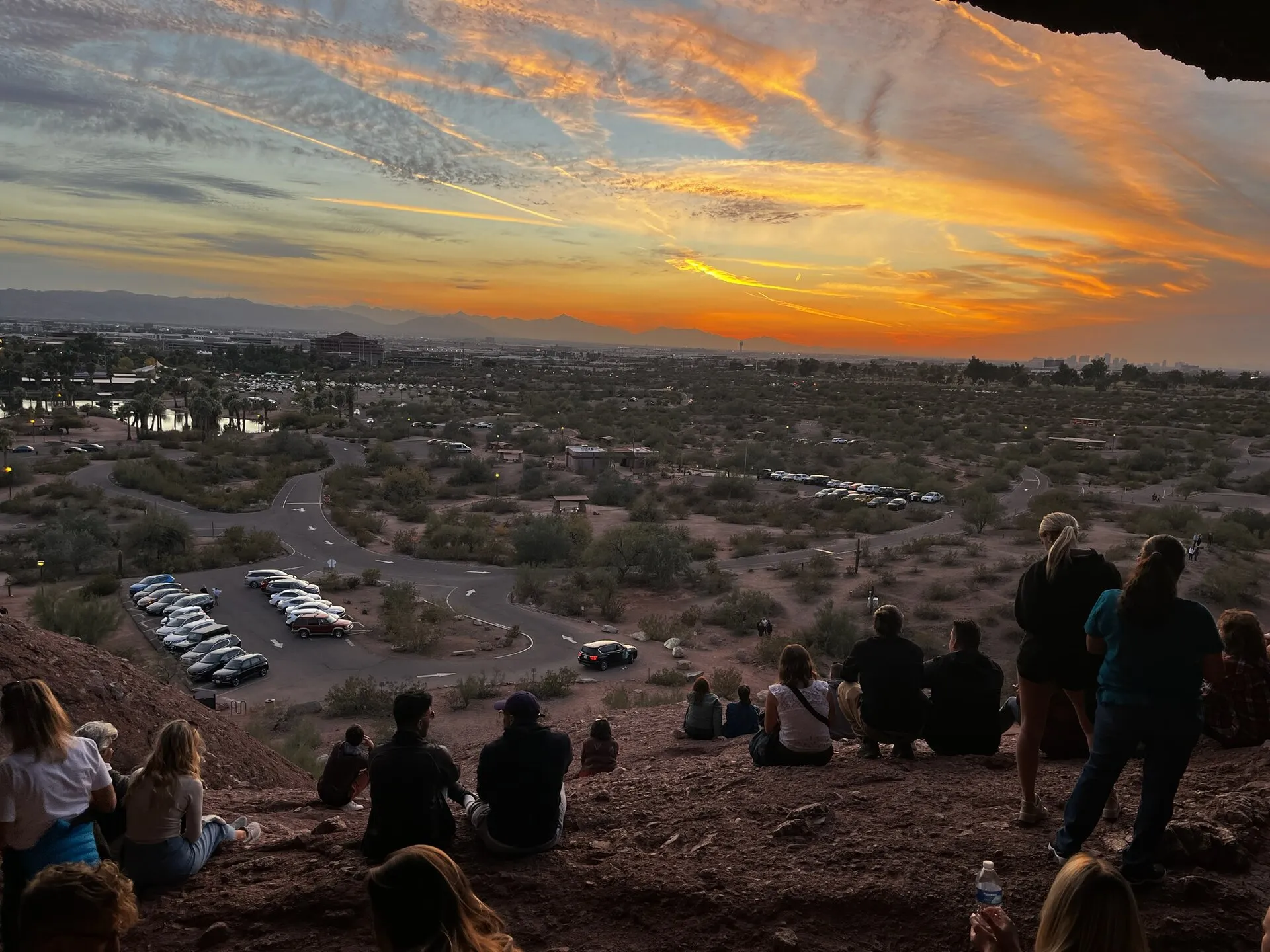 Visitors sitting inside Hole-in-the-Rock at Papago Park watching the sunset over the Valley